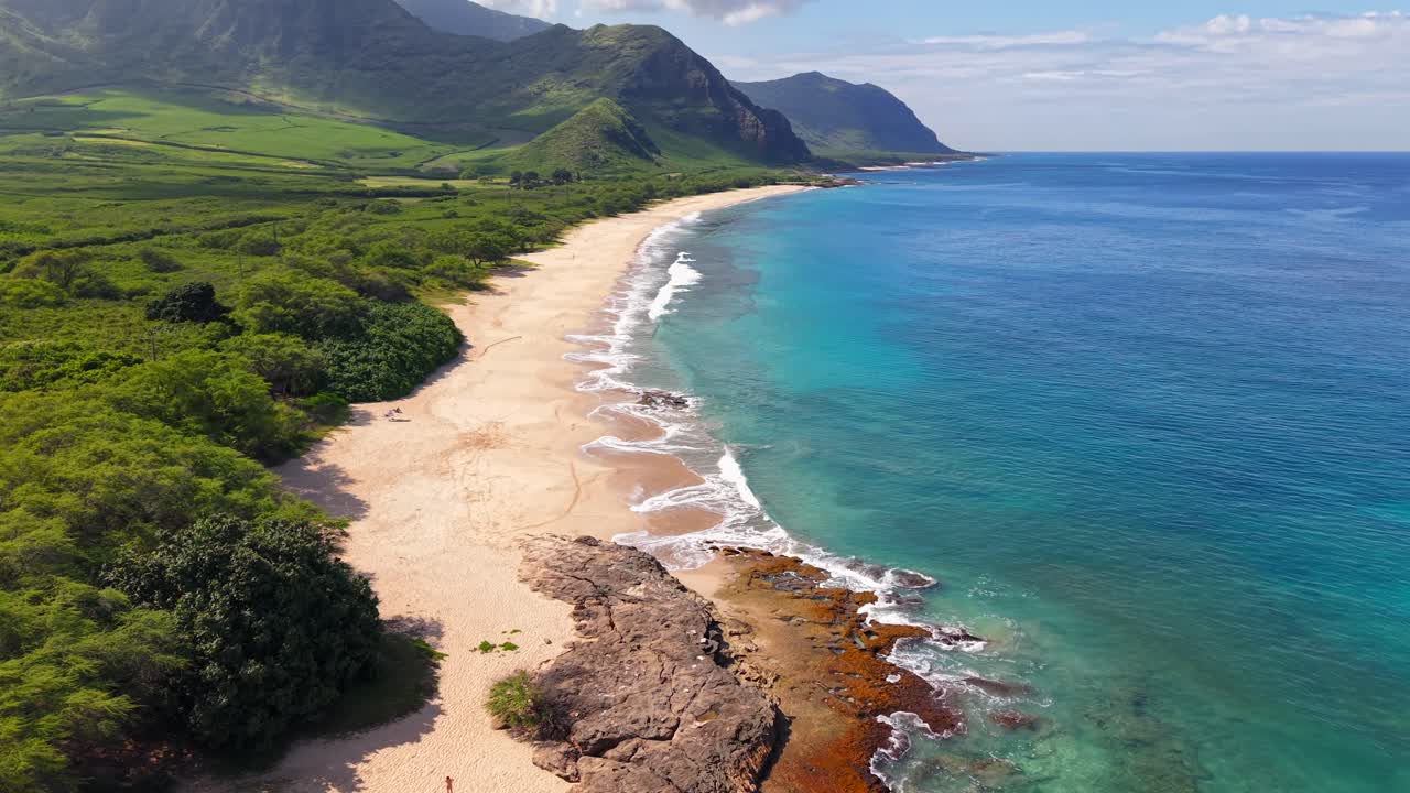Lunga spiaggia sabbiosa con montagne lussureggianti e acqua turchese a Oahu, ripresa aerea in tilt-up