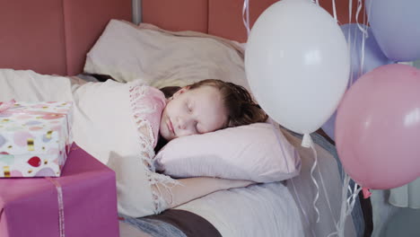 un niño duerme en su cama, al lado de cajas de regalos y globos.