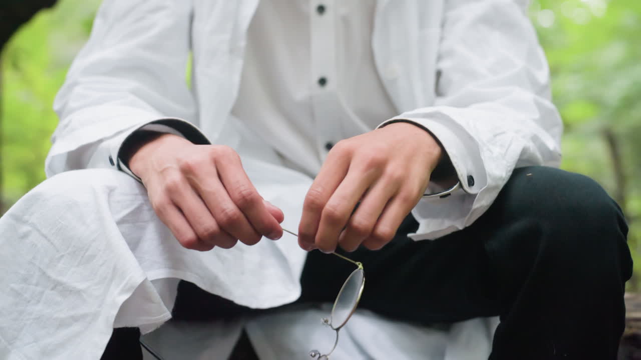 Portrait view young man in white shirt pulling off glasses in forest with tired expression, surrounded by trees, reflecting fatigue during outdoor moment and stress in natural environment