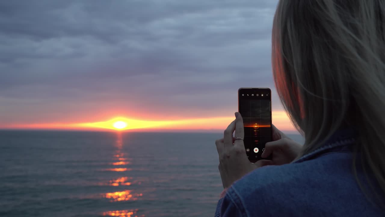 Women's hands hold smartphone and take pictures of sunset on sea