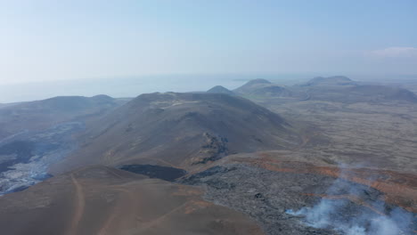 Aerial-drone-view-of-Icelandic-mountains-surrounded-by-black-lava-Fagradalsfjall-fissure-eruption,-forward,-Iceland,-sunny-day