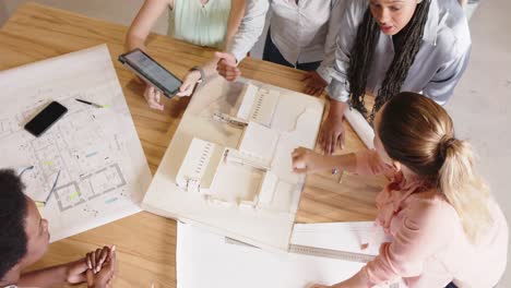 diverse female architects discussing architectural model and blueprints at work, in slow motion