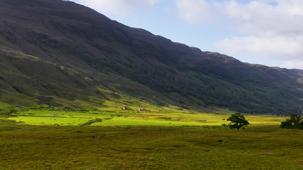 Wide daylight pan over grassy meadow, reflective lake, and distant mountains in Fife, Scotland