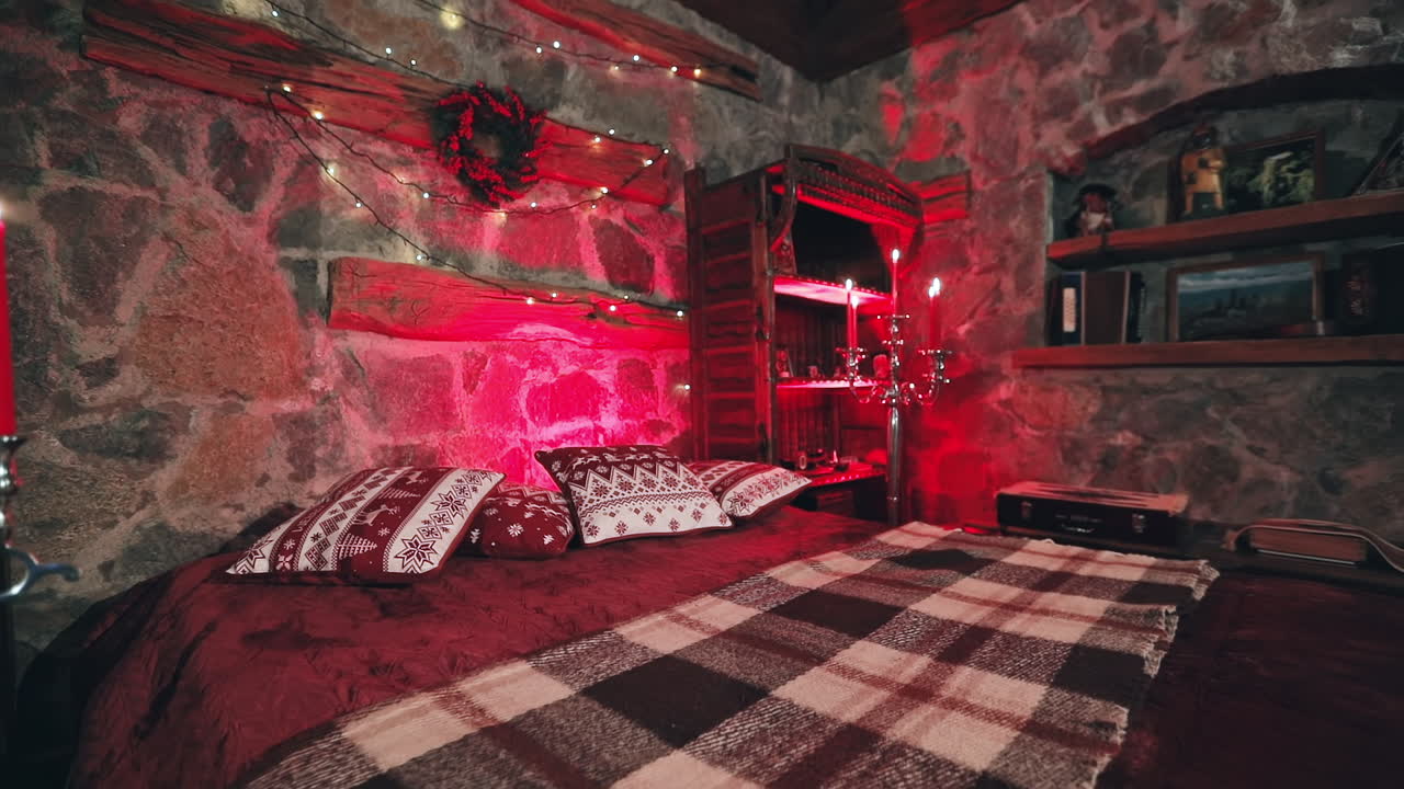 Romantic bedroom at Christmas. Cozy bed and Christmas garland on a wall. Candlesticks with red candles. Christmas decor in the room. Red lighting.