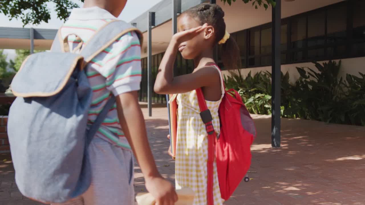 video de un niño y una niña afroamericanos felices con bolsas de escuela dando los cinco fuera de la escuela