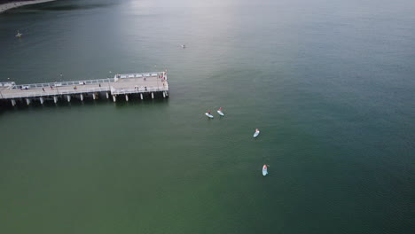 Aerial-flight:-TOurist-on-footbridge-and-sup-paddler-on-Baltic-Sea-in-Gdynia-Orlowo-during-sunlight