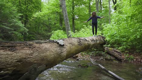 Ein-Mädchen-Balanciert-Auf-Einer-Holzbrücke,-Während-Sie-Beim-Wandern-Einen-Kleinen-Bach-überquert