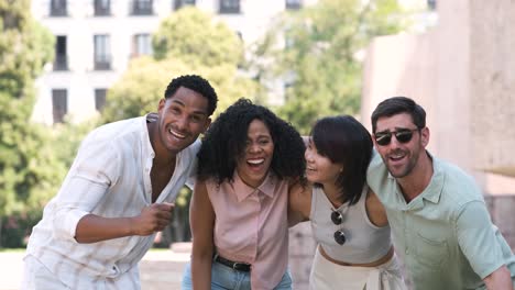 cheerful friends laughing while standing arms around at city park during daytime