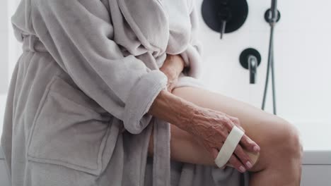 close up of unrecognizable senior woman doing peeling of her legs in the domestic bathroom