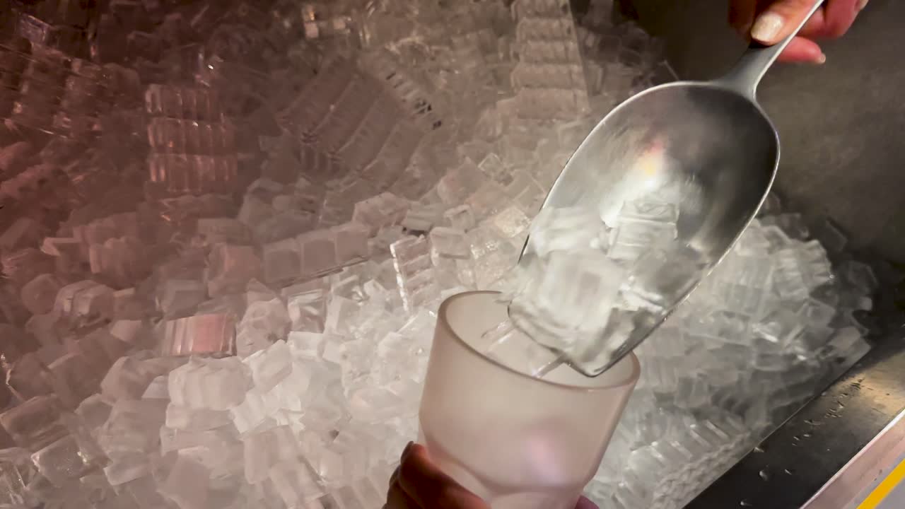 A person scoops ice into a cup from a large ice bin in a dimly lit setting