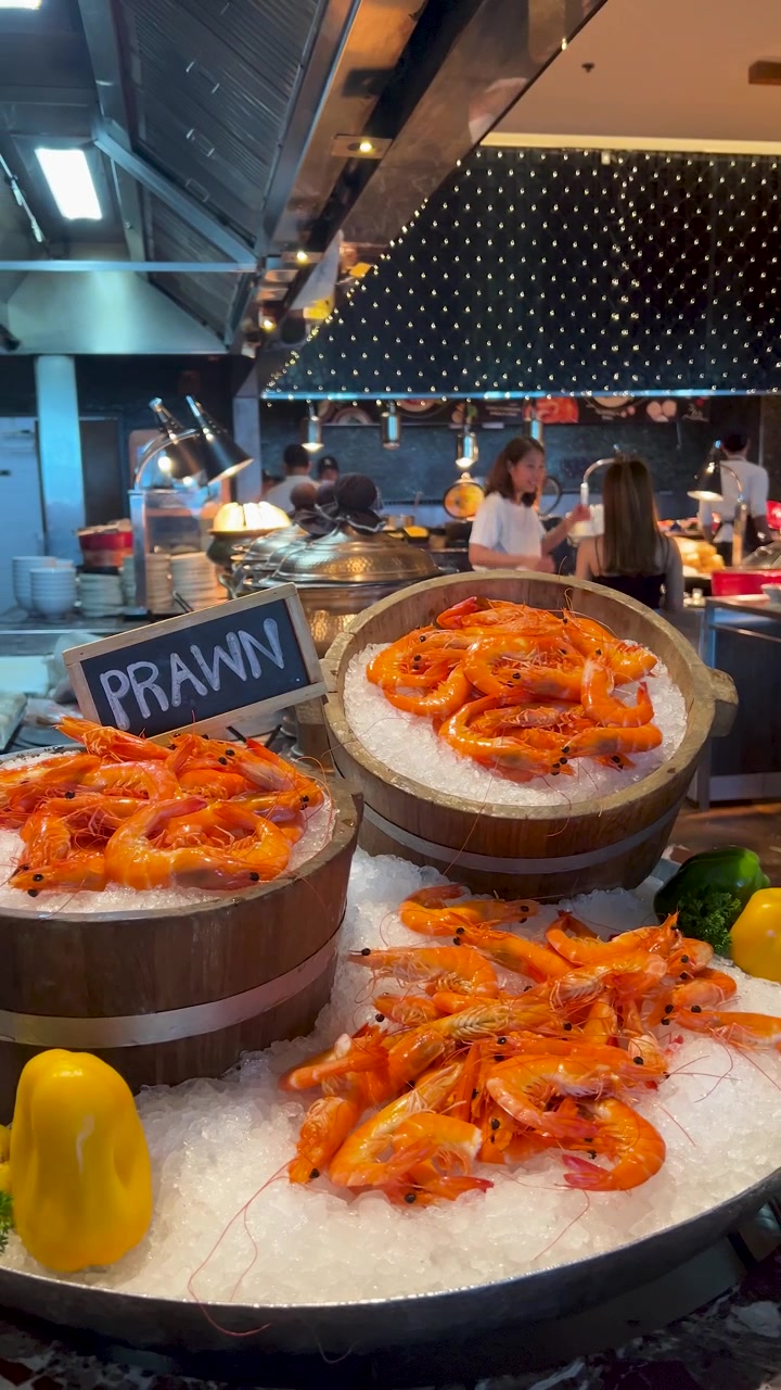 Gamberi cotti adagiati su ghiaccio tritato in secchi di legno presso una trafficata stazione buffet di un ristorante.