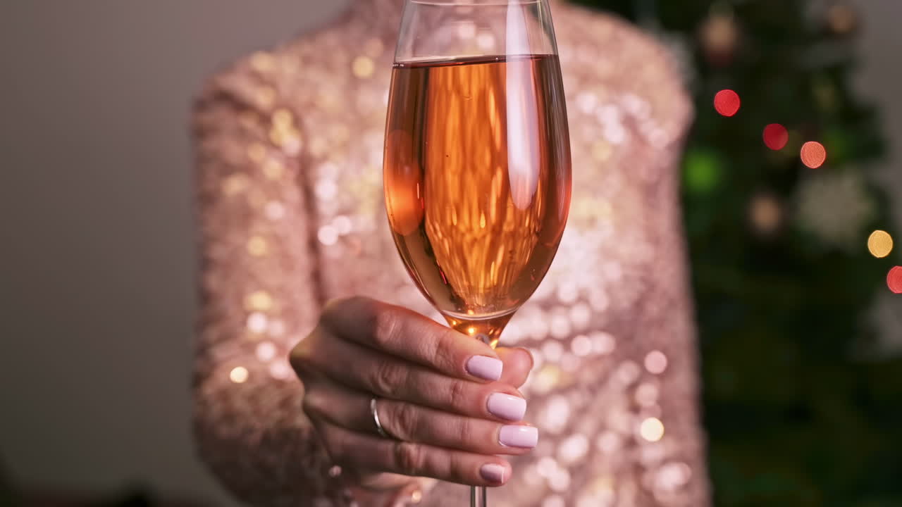 Shiny dressed woman holding a glass with champagne and shows it to the camera