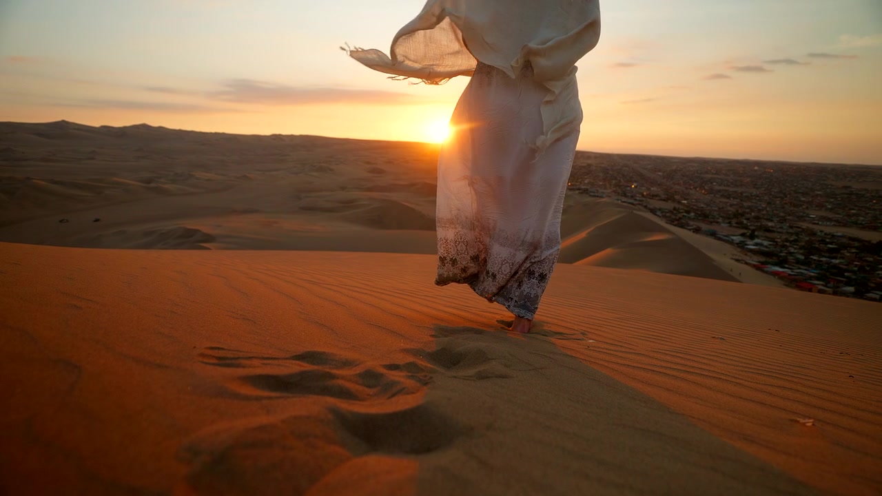 Viaggiatrice con un abito svolazzante in cima a una duna a Huacachina cammina verso il tramonto.