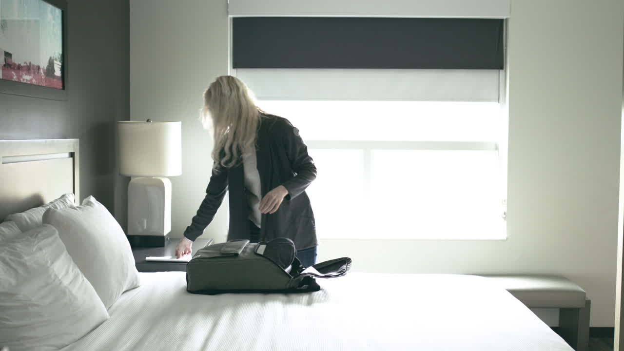 A young blonde millennial packs her bag in her bedroom as she prepares to leave for work shot handheld in UHD 4K