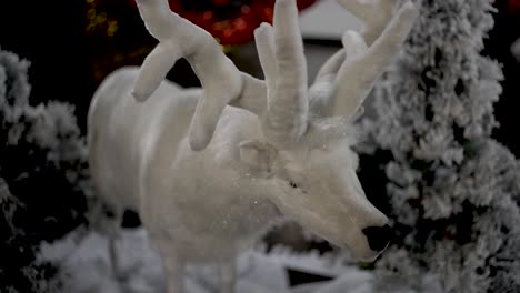 white plush reindeer christmas ornament with snowed artificial trees behind, close up shot