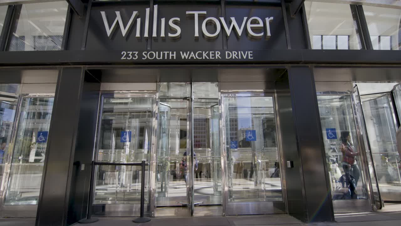People entering and exiting the iconic Willis Tower through its revolving doors on a sunny day in Chicago