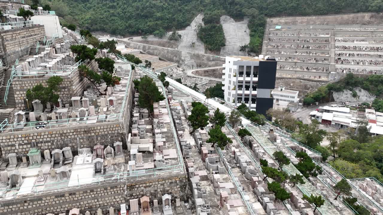 Ripresa aerea con drone del Cimitero di Pok Fu Lam a Hong Kong, con tombe collinari, vegetazione lussureggiante e un paesaggio urbano panoramico in un contesto tranquillo e suggestivo.