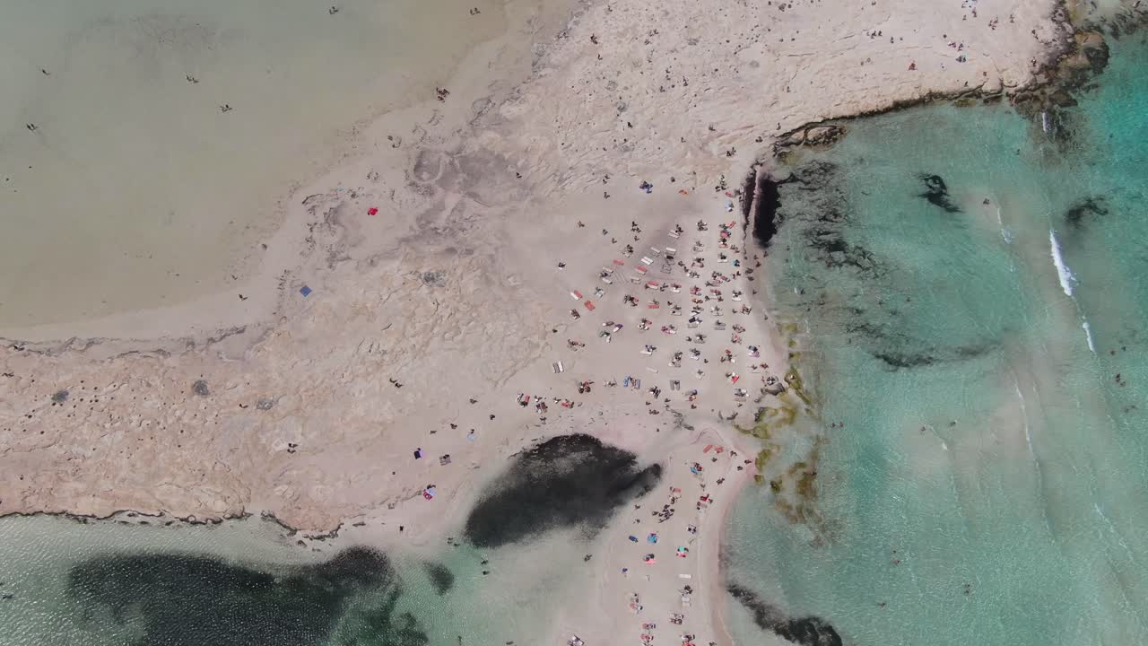 그리스의 드론 뷰: 크레타의 빛 날에 수영하는 사람들과 함께 은 파란 바다와 에 은 모래를 가진 발로스 해변의 상단 뷰