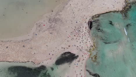 Vista-De-Drones-En-Grecia-Vista-Superior-Sobre-La-Playa-De-Balos-Con-Mar-Azul-Claro-A-Los-Lados-Y-Arena-Blanca-Con-Gente-Nadando-En-Un-Día-Soleado-En-Creta