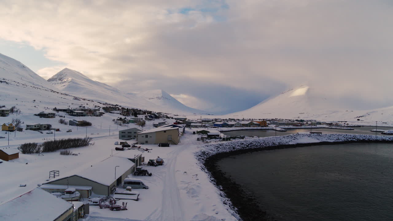 Coastal Icelandic building surrounded by snowy plains, under soft Arctic light, aerial ascend over industrial harbor in winter