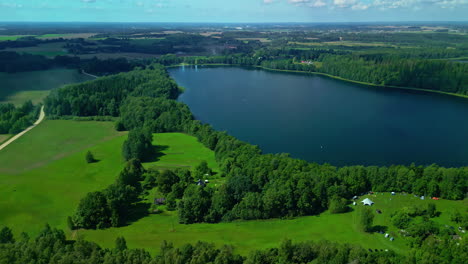 lake flyover aerial, tilt up to cloudy sky, idyllic rural area, green meadows, big water pond, blue sky with peaceful clouds, drone landscape overview of the countryside