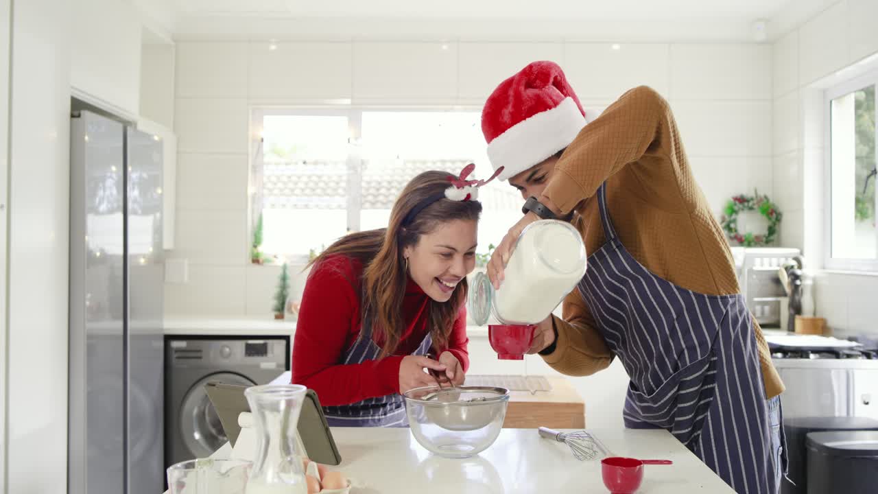 Following tablet recipe African American couple at kitchen island pouring flour and whisking batter