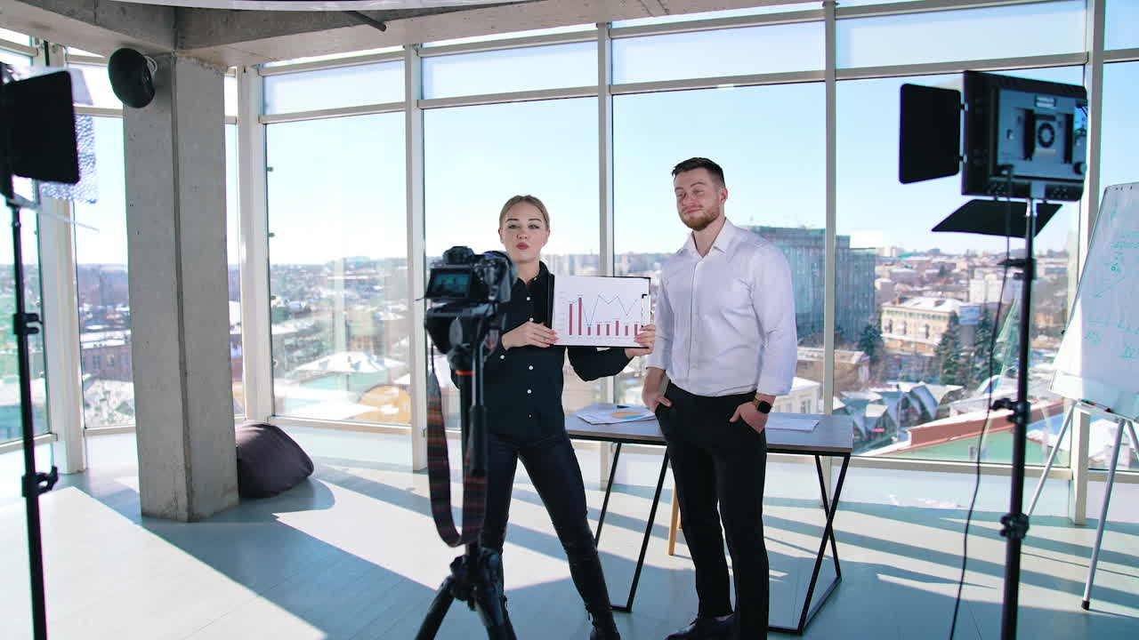 Young business people talking about new strategy. Attractive female holding graphics of business project and speaking on camera in office room.
