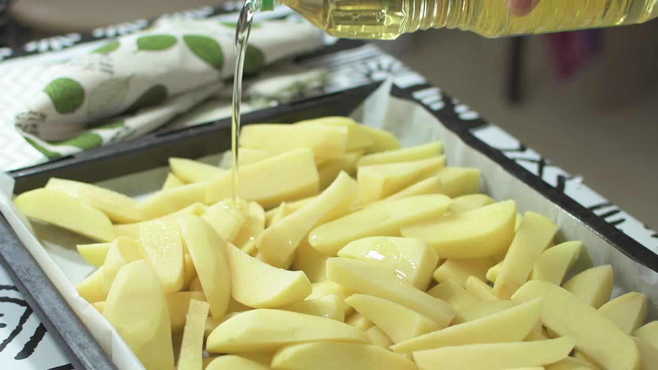 Putting oil on cut potatoes in a tray, to cook them in the oven.