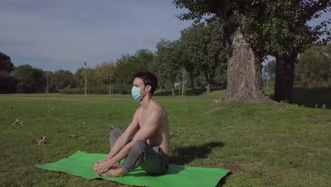 Close-up-dolly-of-young-athlete-man-with-mask-doing-exercises-on-the-mat-in-the-nature,-healthy-workout