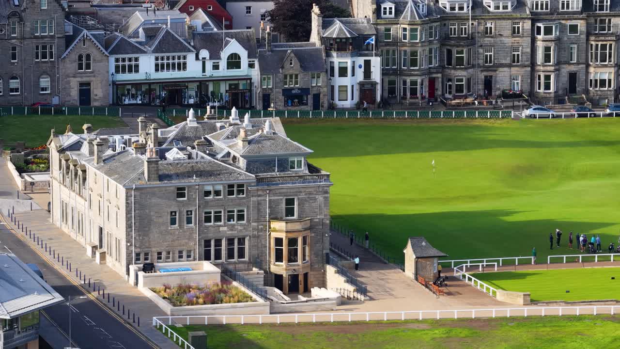 Drone captures golfers playing on putting green near iconic clubhouse in bright daylight