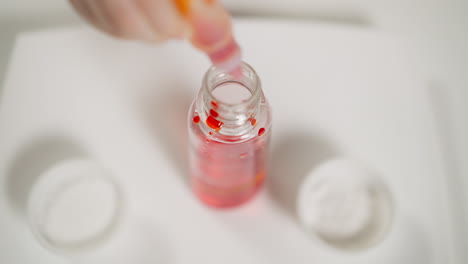 Little-girl-drips-red-paint-into-glass-bottle-from-tube