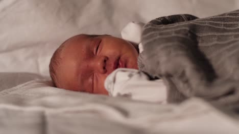 close up of newborn baby boy laying and settling on sofa in living room covered with gray blanket