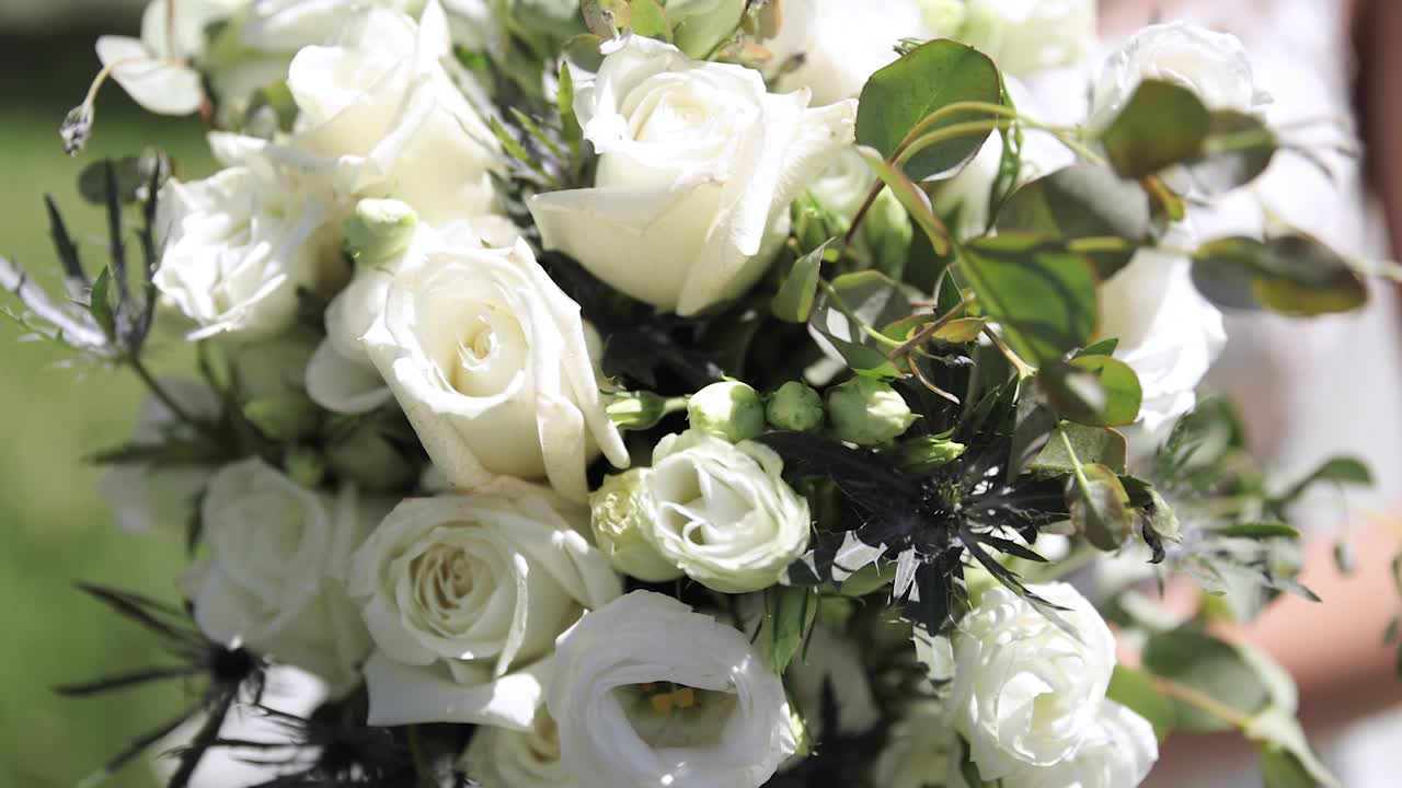 하얀 장미와 녹지 1080p 60fps로 야외에서 큰 꽃 결혼식 부케를 들고 있는 웨딩드레스를 입은 신부를 닫습니다