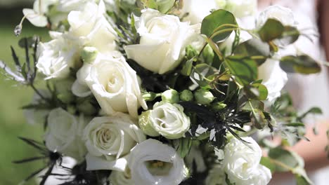 close up of bride in her wedding dress holding large flower wedding bouquet in her hands outdoors with white roses and greenery 1080p 60fps