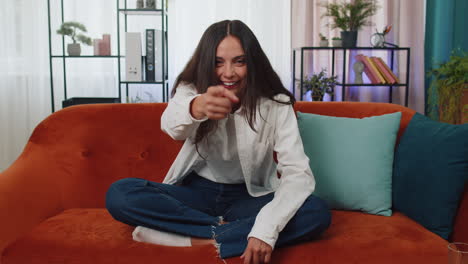 mujer joven sonriente apuntando a la cámara, eligiendo al afortunado ganador, indicando, invitando, aprobando en casa