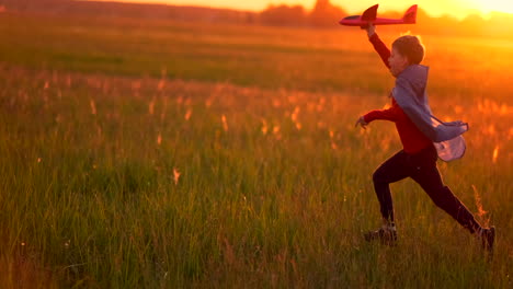 a happy boy with a raincoat imagines himself an airplane pilot and runs with a toy across the field thinking that he is an airplane pilot at sunset.