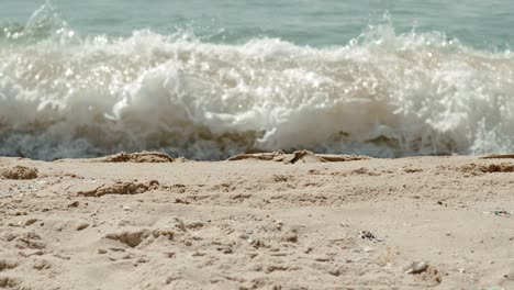 close-up on the sand of the shore of israel's blue mediterranean coast when the waves hit the distant breakwater, people in the water and a long antenna can be seen in the view