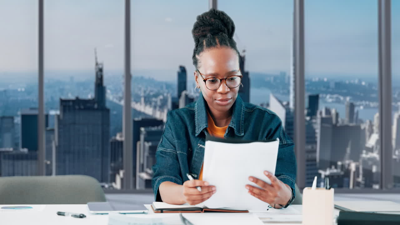 Young Black Woman Reading Documents at Office Desk with City View