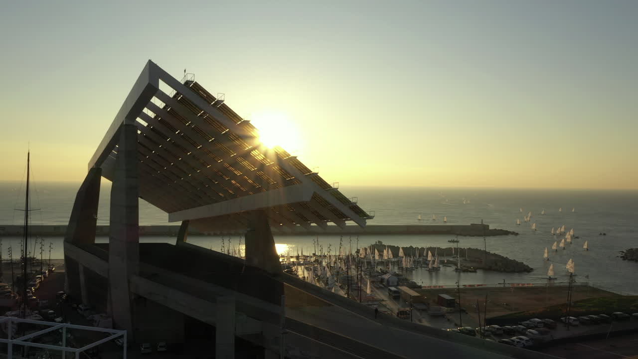 sol desapareciendo detrás de la estructura del panel solar del puerto deportivo de barcelona en el parc del forum a la hora dorada