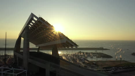 sun disappearing behind barcelona marina solar panel structure in parc del forum at golden hour