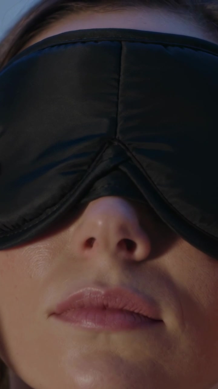 Vertical video: Breathing causing woman shifting black padded eye mask at home, settling on nose