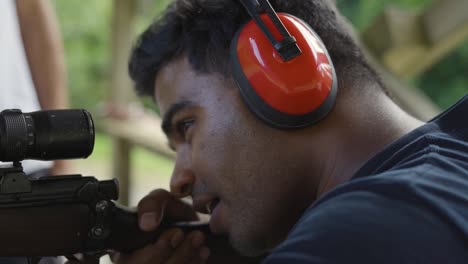 closeup of man looking through magnification scope of rifle at firing range