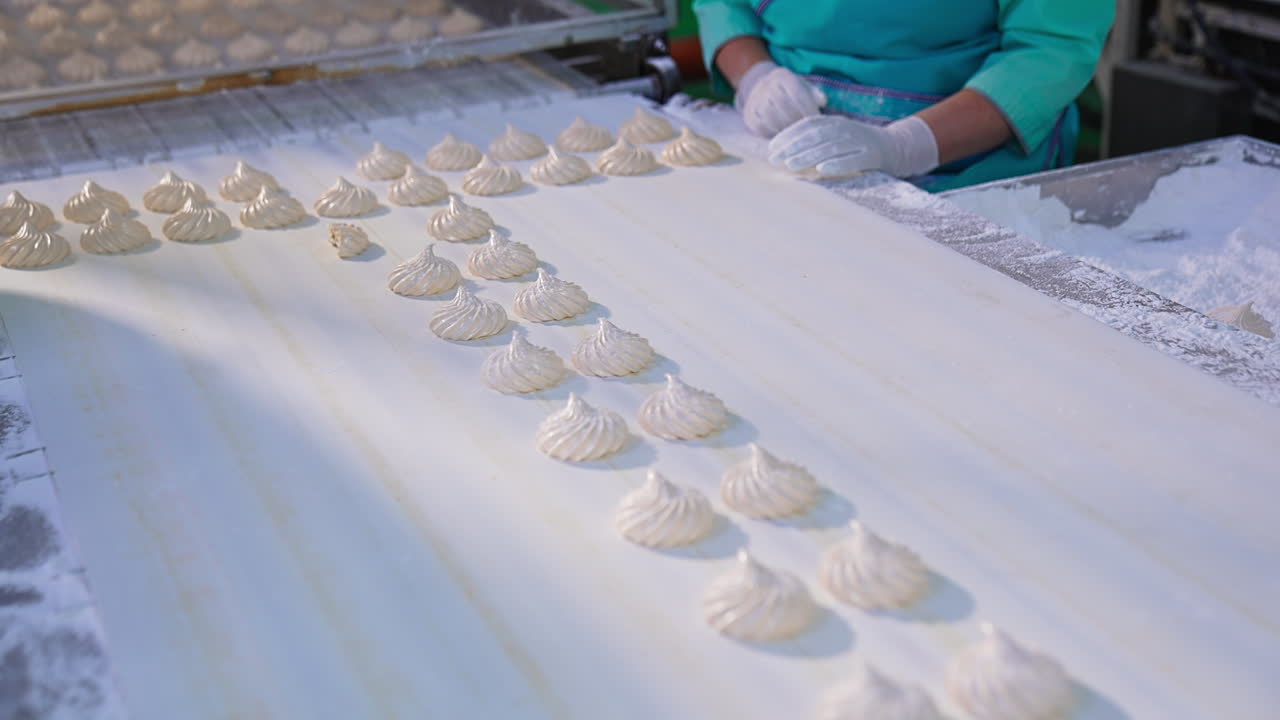 Creamy marshmallows move along the white conveyor belt. Confectionery workers stand by the conveyor. Close up.
