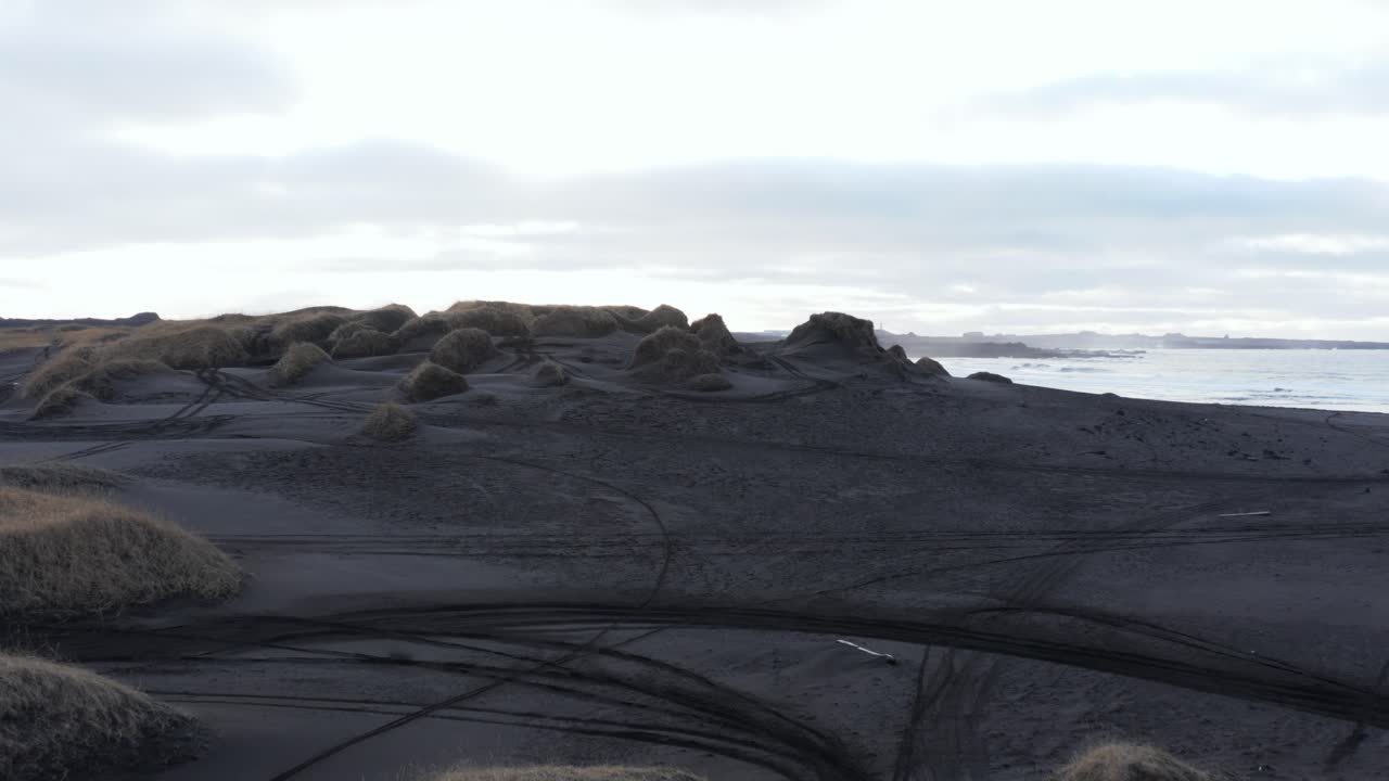 dunas cubiertas de hierba con arena negra volcánica en la cala costera de sandvik, antena