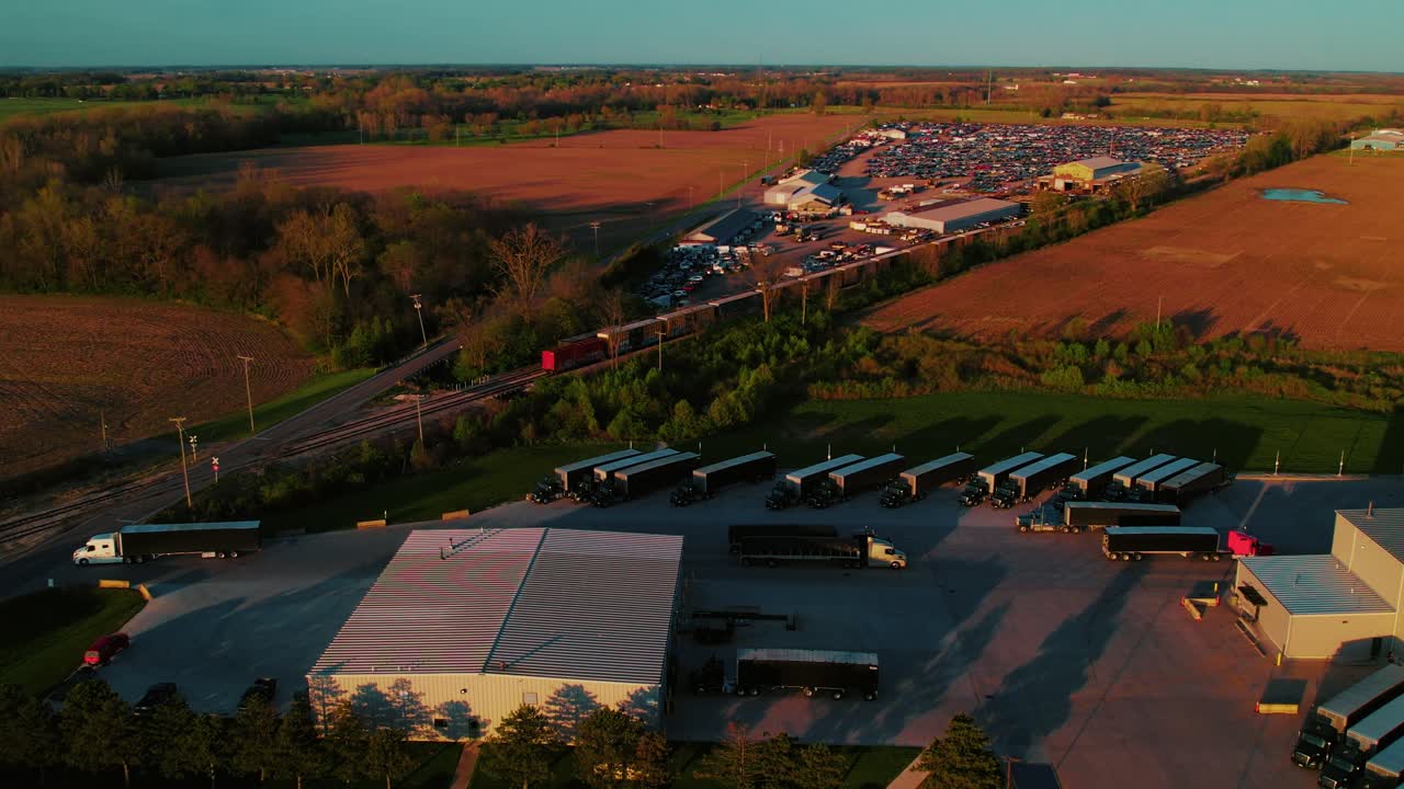 Drone view over Kenton, Ohio shipping hub with multiple parked trucks, freight activity, and rural farmland during golden hour. Connestoga trailers.