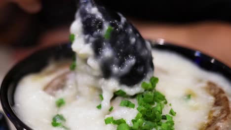 a close-up view of creamy porridge topped with fresh green onions, served in a black bowl.