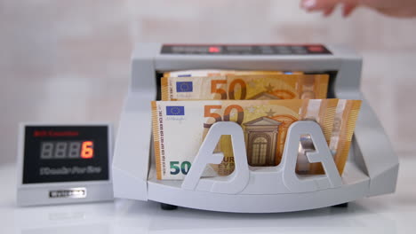 electronic device is calculating fifty-euro bills. woman puts paper banknotes into automatic counting machine. automatic mechanism for bank financial operations. currency exchange.