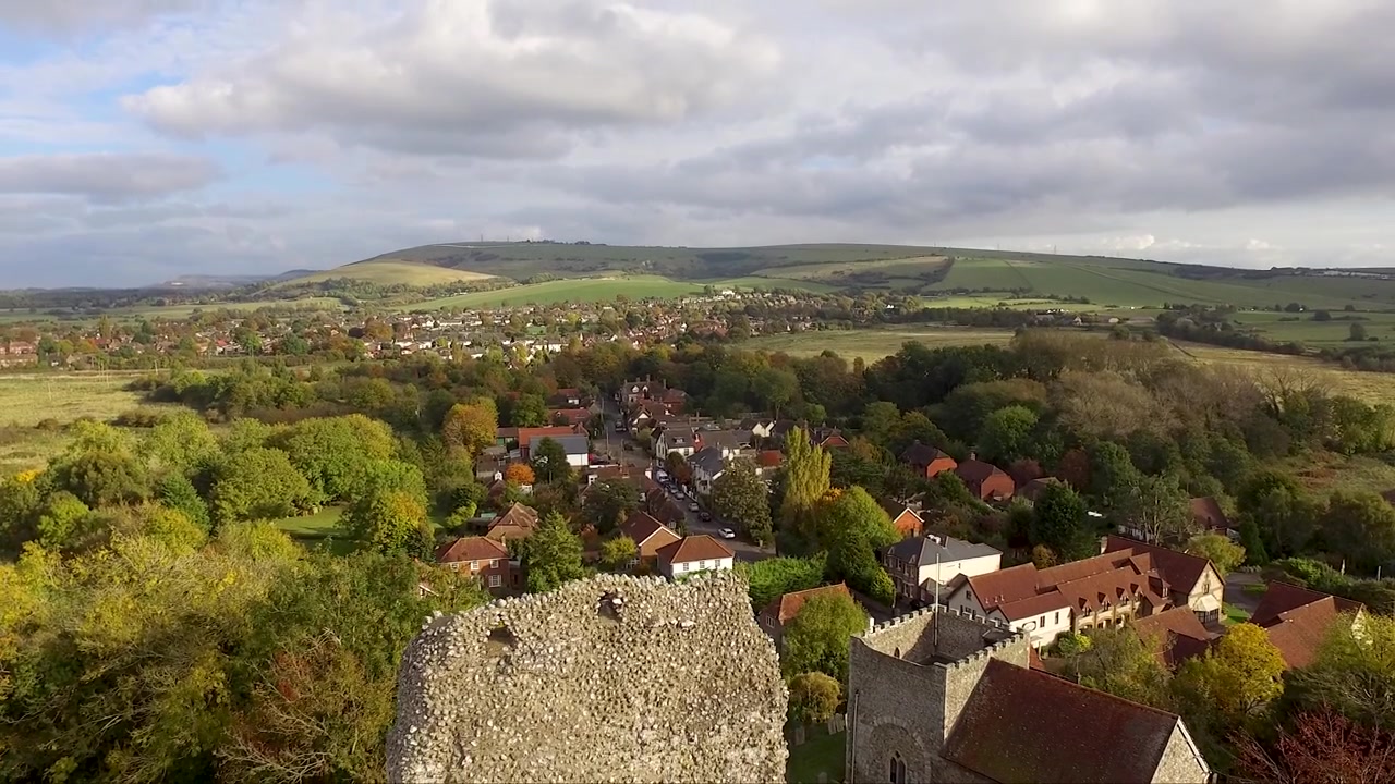 Ripresa con drone di un villaggio di campagna nel Regno Unito, sovrastato dalle rovine di un antico castello medievale.