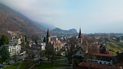 Aerial-pullback-leaves-cathedrals-and-chapel-with-view-of-Interlaken-Switzerland-homes-sprawling-in-the-distance