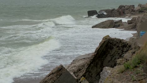 Big-stormy-waves-breaking-against-abandoned-seaside-fortification-building-ruins-at-Karosta-Northern-Forts-in-Liepaja,-Baltic-sea-coastline,-wave-splash,-overcast-day,-wide-angle-shot